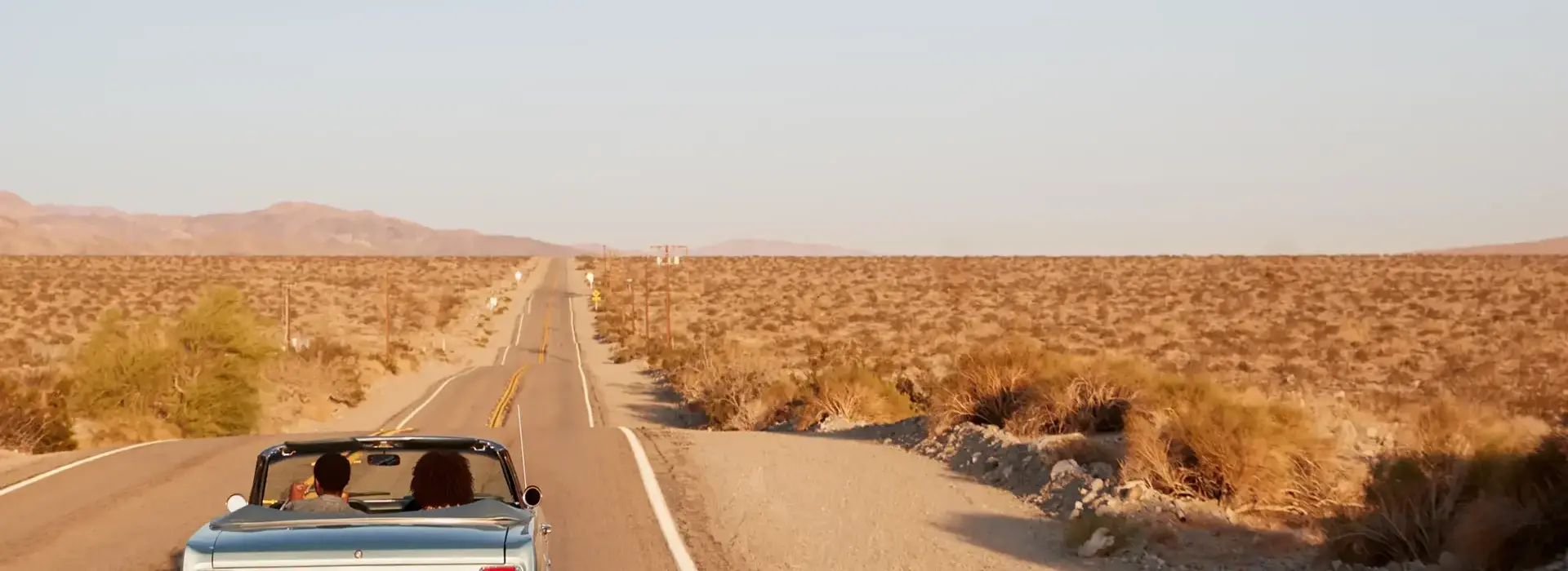 Couple driving convertible car on desert highway, back view