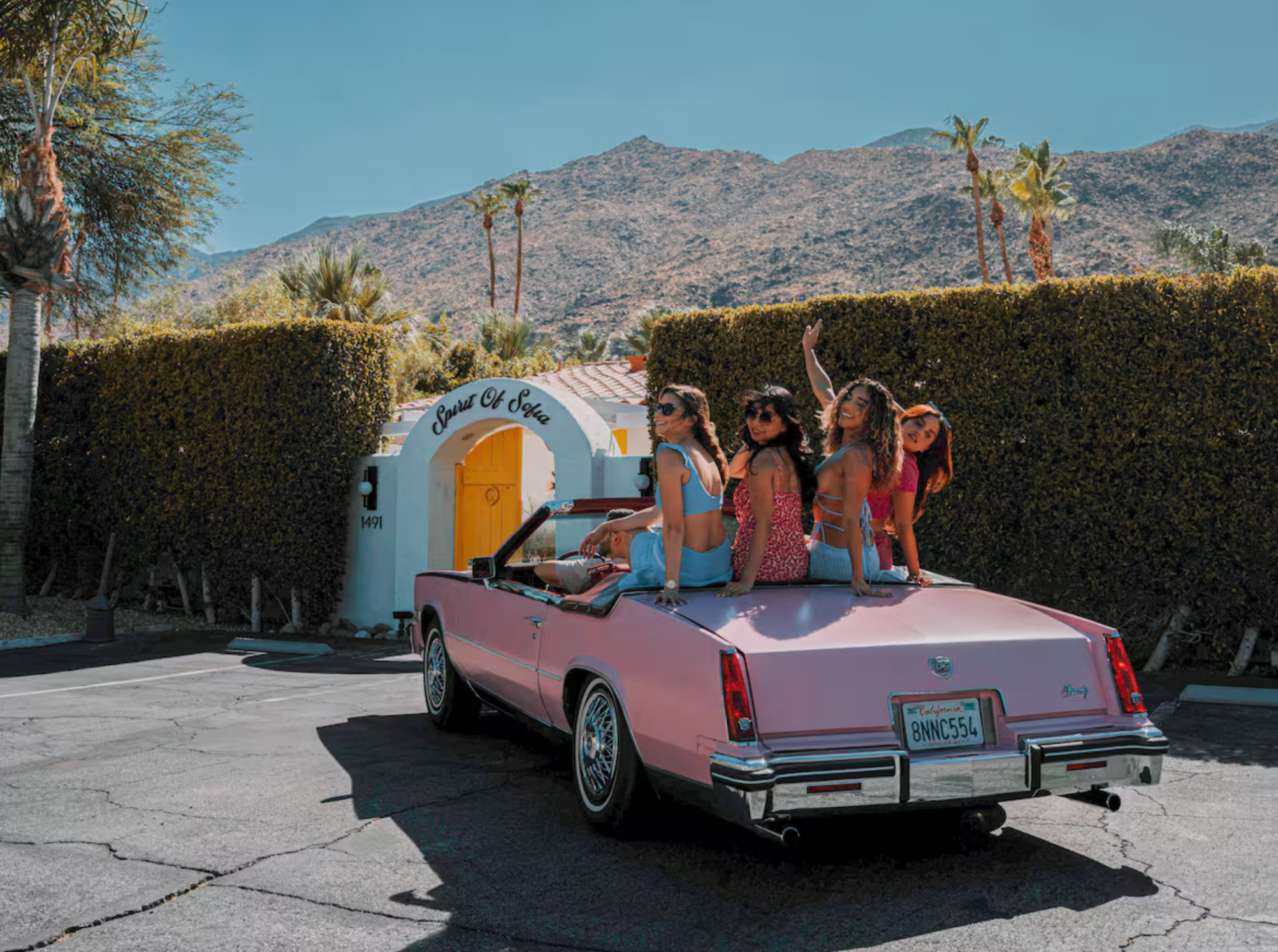 four women sitting on the back of a pink convertible outside of the Spirit Of Sofia vacation rental, waving
