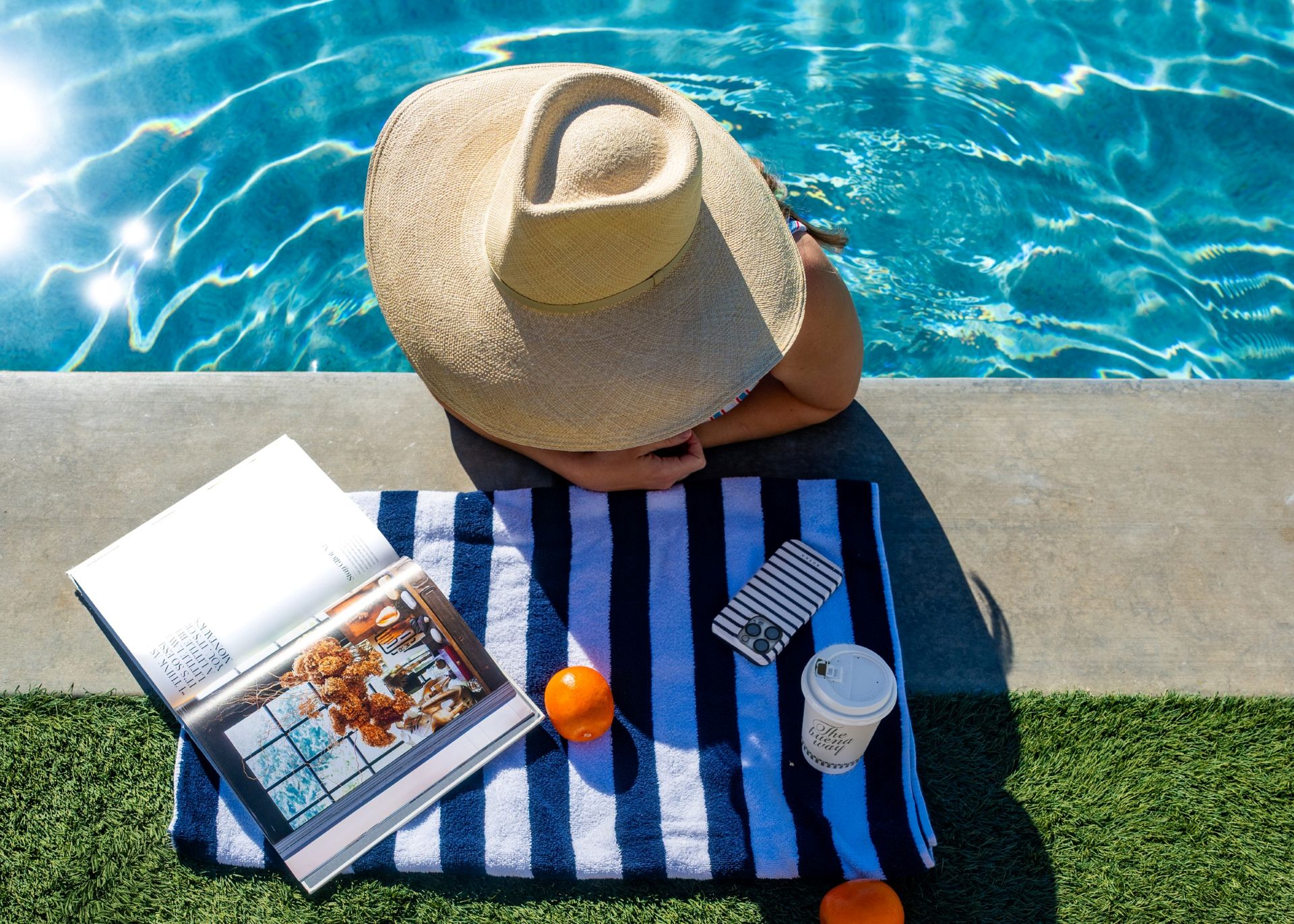 a top-down view of a woman wearing a sunhat and reading in a pool