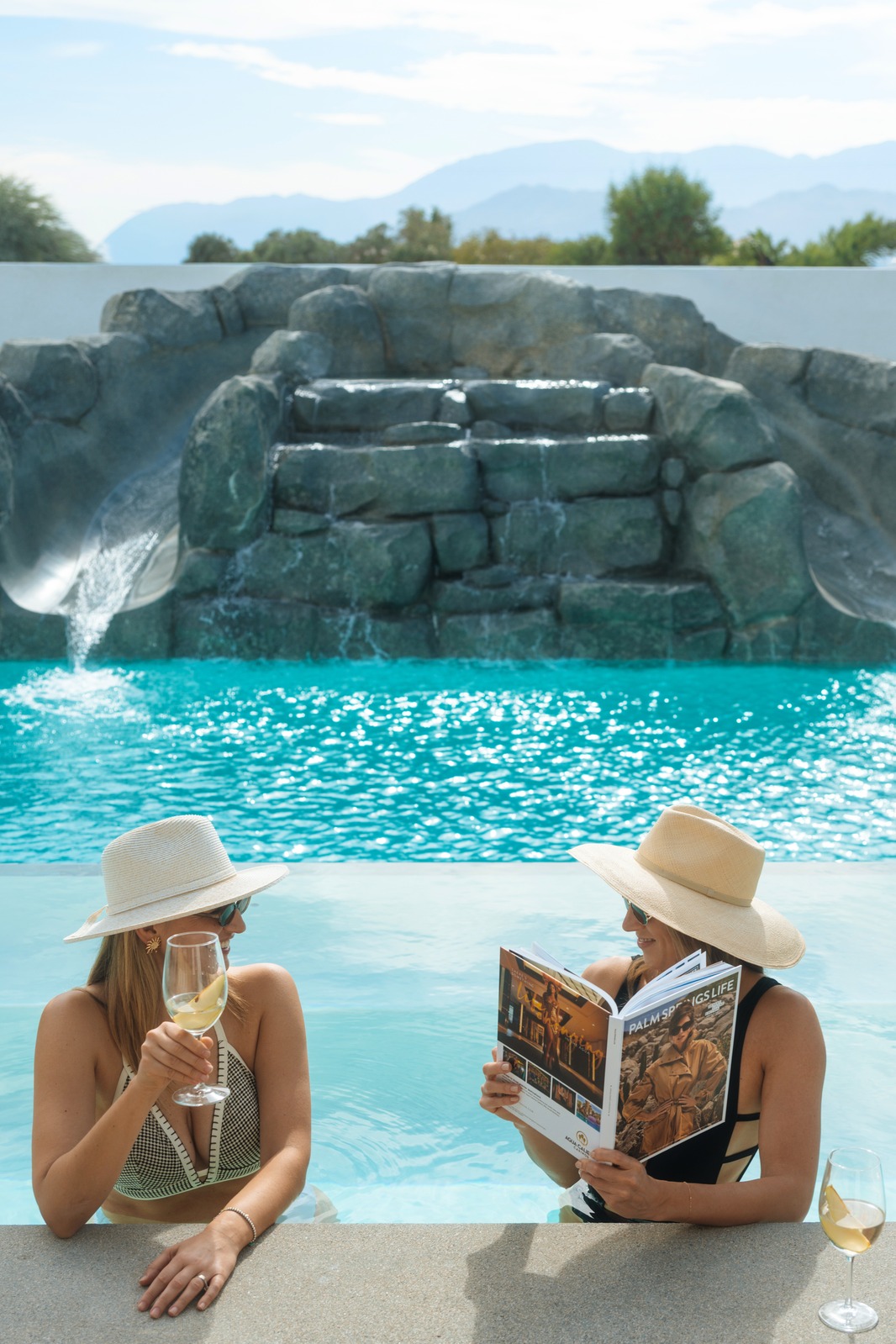 Two women relaxing by the pool with drinks and a magazine